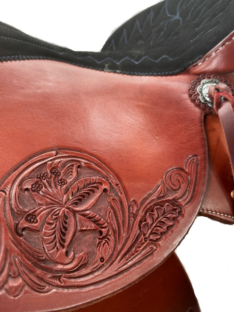 Close-up of a brown leather saddle with intricate floral tooled design.